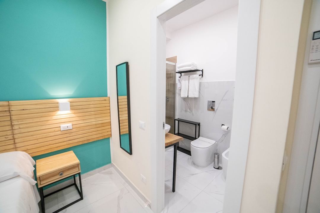 Modern hotel room featuring a turquoise accent wall, wooden headboard, and an ensuite bathroom with white marble tiles.