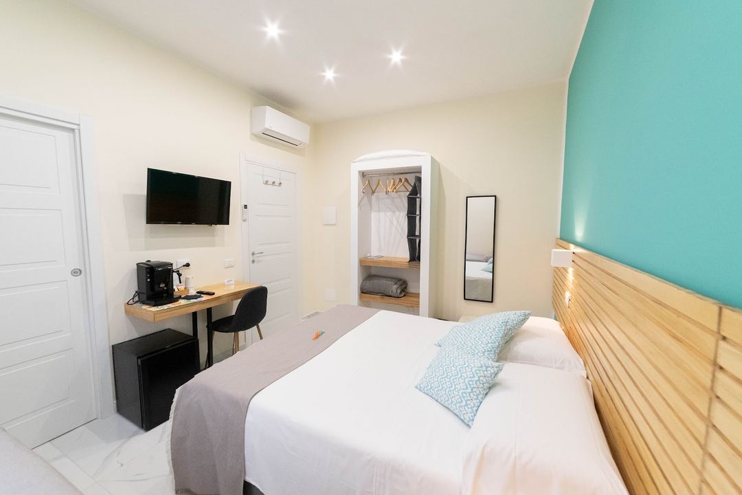 A modern bedroom with turquoise accent wall, wooden furnishings, queen bed, work desk, and ensuite wardrobe at Mandra B&B.